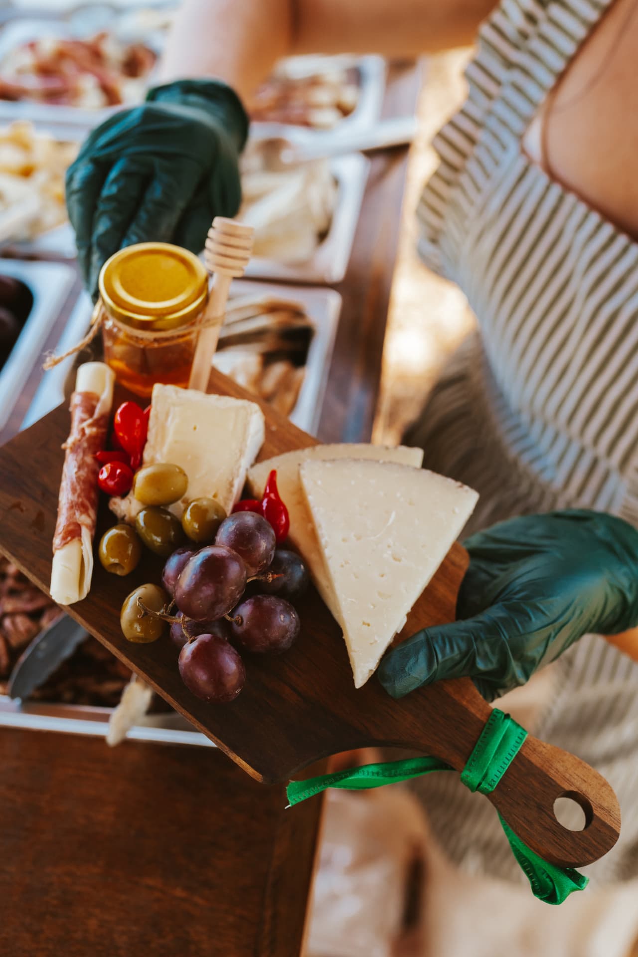 An attendant presenting a finished charcuterie board with cheese, grapes, olives and honey