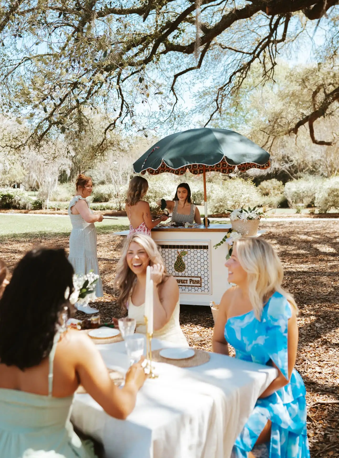 Friends celebrating at a garden table beside The Perfect Pear cart